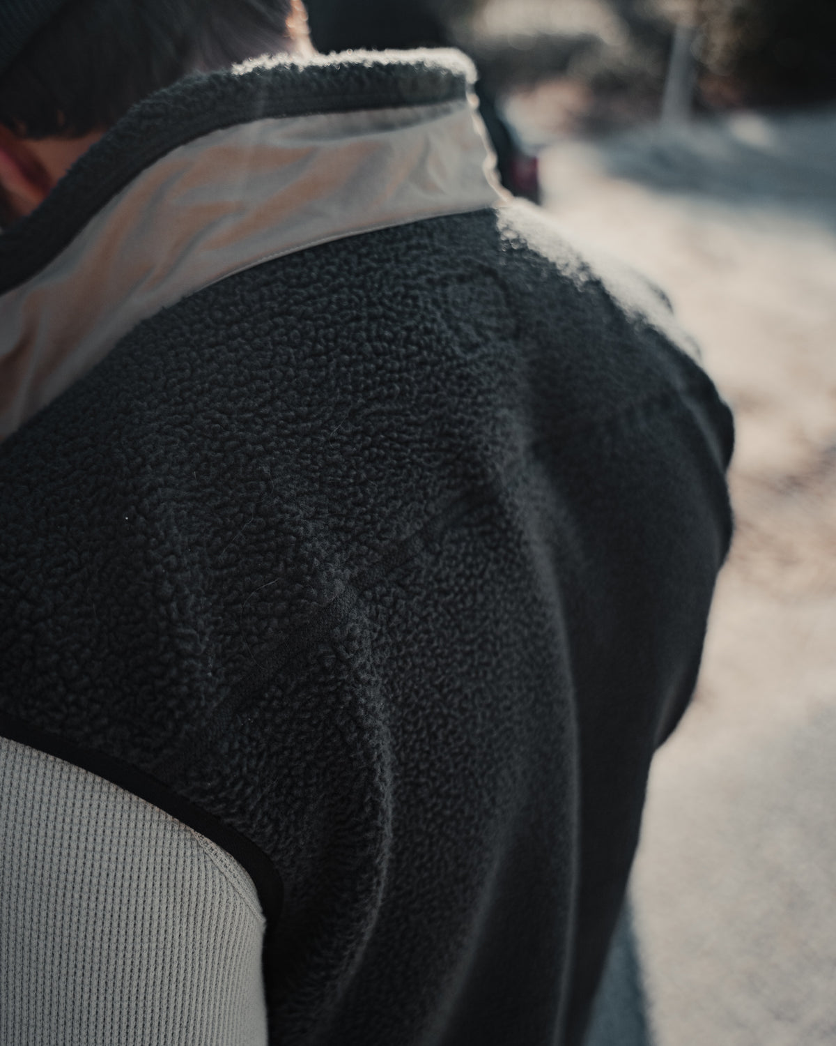 Close-up of a person wearing the Choona Pt. Washington Sherpa Vest with a light beige collar. The photo is taken outdoors in natural daylight, featuring a softly blurred background.