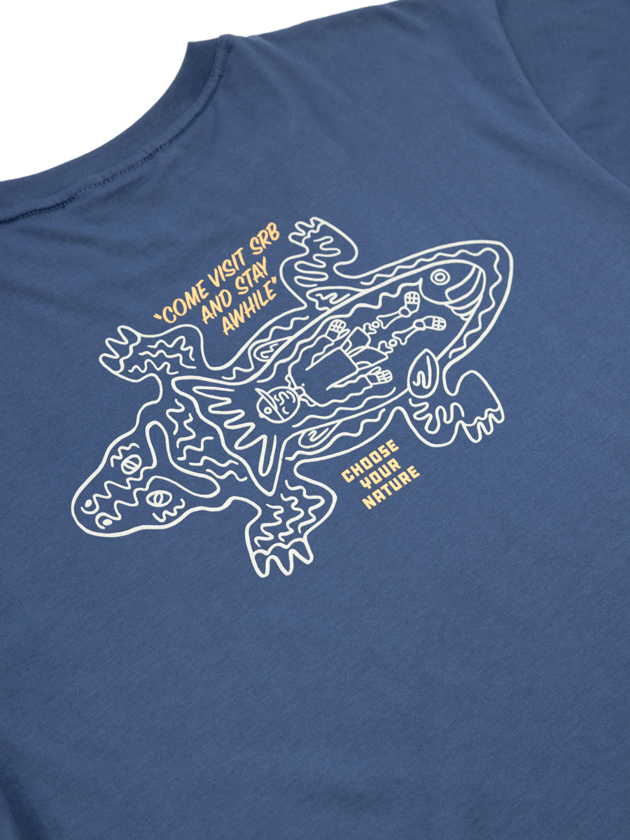The Choona Stay Awhile Graphic Tee is made from 100% Pima Cotton and features a white lizard and person line drawing with “COME VISIT SBB AND STAY AWHILE” and “CHOOSE YOUR NATURE”—ideal for outdoor lifestyle enthusiasts.