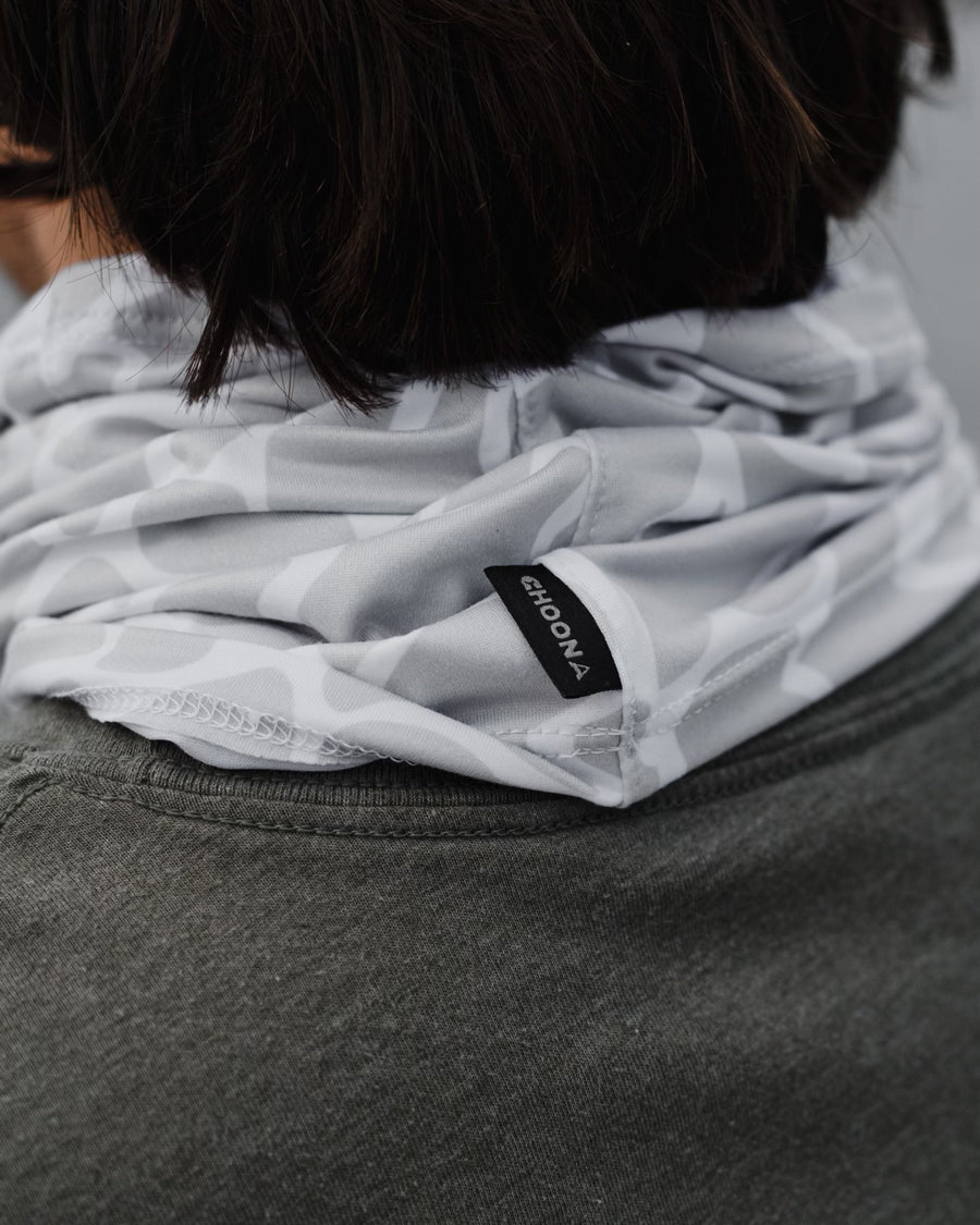 Close-up of a person wearing the Choona Grayton Sun Mask, an ultra lightweight grey neck gaiter with a geometric pattern and visible black CHOONA tag, paired with a dark grey shirt for outdoor protection.