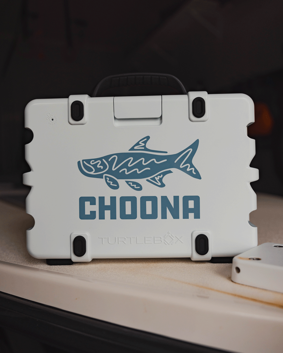 A Choona Tarpon Decal by Choona is displayed on a white Turtlebox case with black latches, featuring a blue fish design, bold CHOONA lettering, and an adventure-ready look on a beige surface.