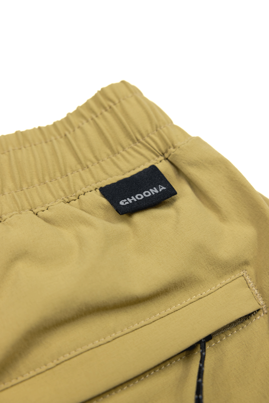 Close-up of light tan Shore Short by Choona featuring an elastic waistband and a black label above the back pocket. Visible stitching and subtle wicking technology make it perfect for coastal activities.
