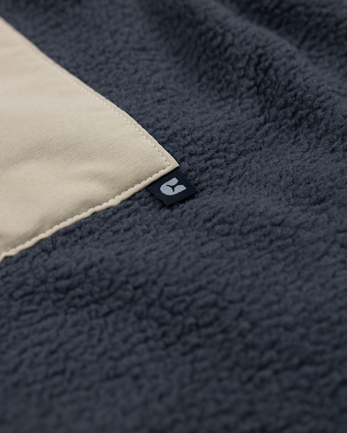 Close-up of the Choona Pt. Washington Sherpa Vest in dark gray high pile fleece, featuring a beige rectangular patch and a small black tag with a white logo for a cozy look.