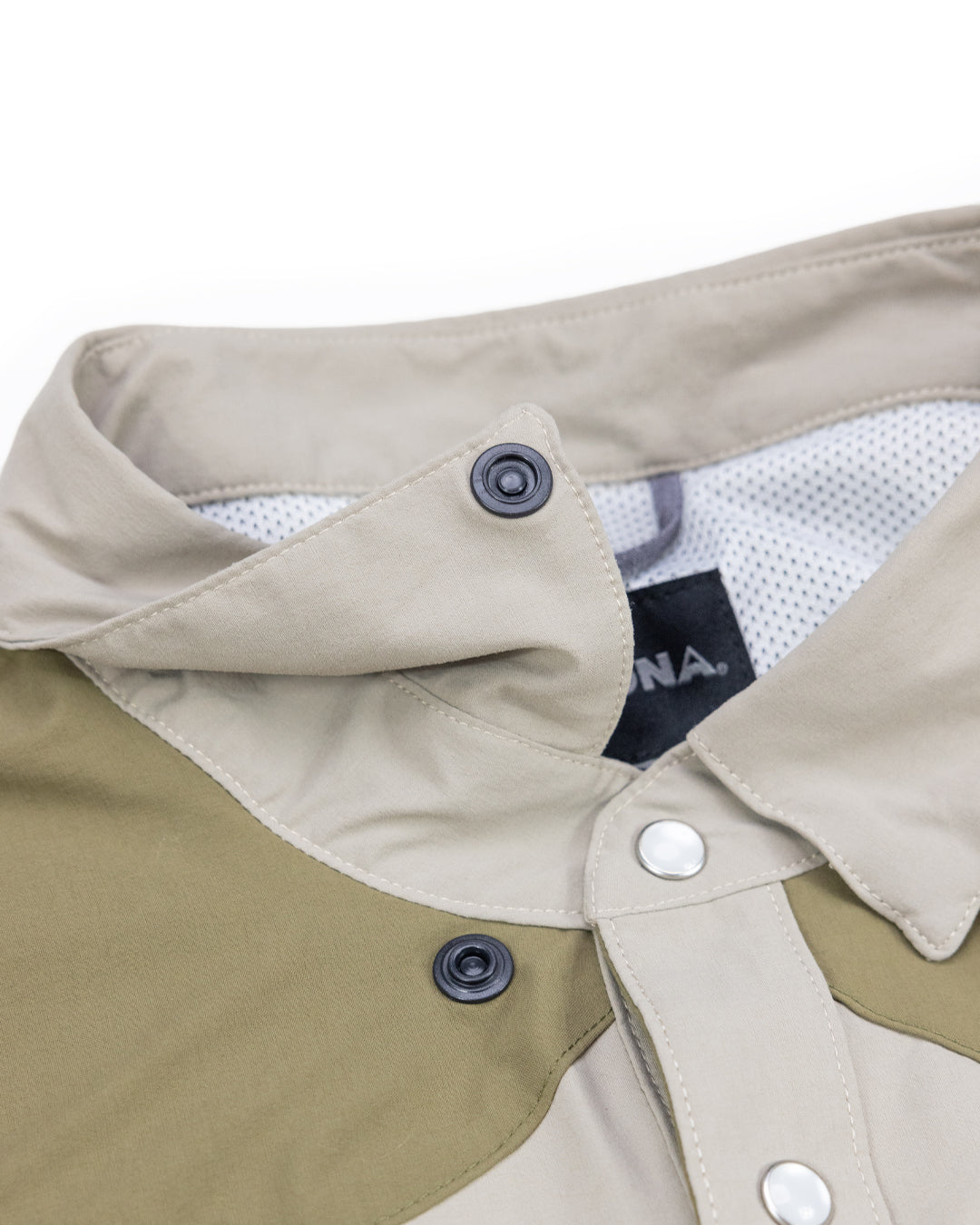 Close-up of the Choona Panhandle Pearl Snap shirt, featuring beige and olive green panels, black buttons, mesh inner lining, and a black tag—offering a modern twist on coastal cowboy style.
