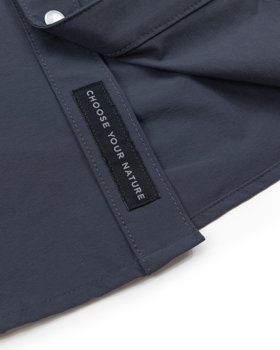 A close-up of the Panhandle Pearl Snap by Choona shows dark blue fabric and a black label with CHOOSE YOUR NATURE in white. This shirt captures a coastal cowboy vibe, ideal for the Florida Panhandle.