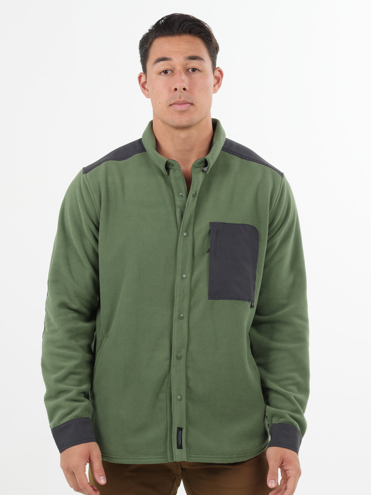 A man wears the Choona Skipper Shacket—a green fleece jacket with recycled polyester and dark gray accents on the shoulders, pocket, and cuffs—standing against a plain white background. Perfect for cold weather.