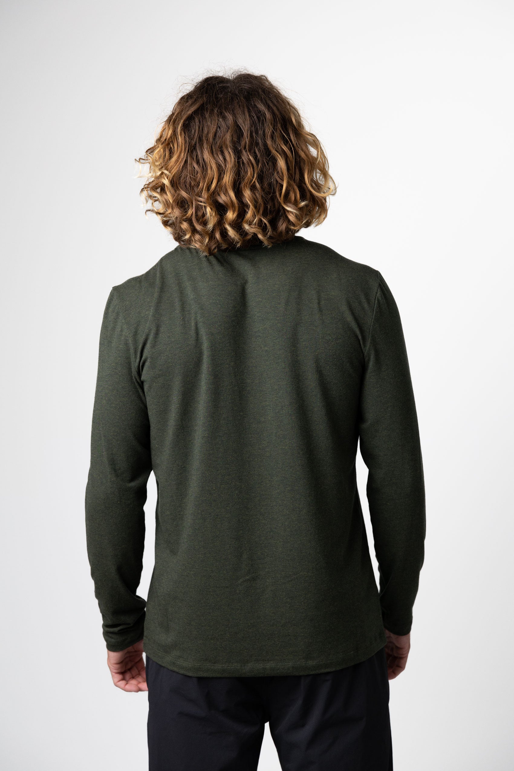 A person with shoulder-length curly hair stands with their back to the camera, wearing the Choona Versatile LS Henley with black pants, set against a plain white background.