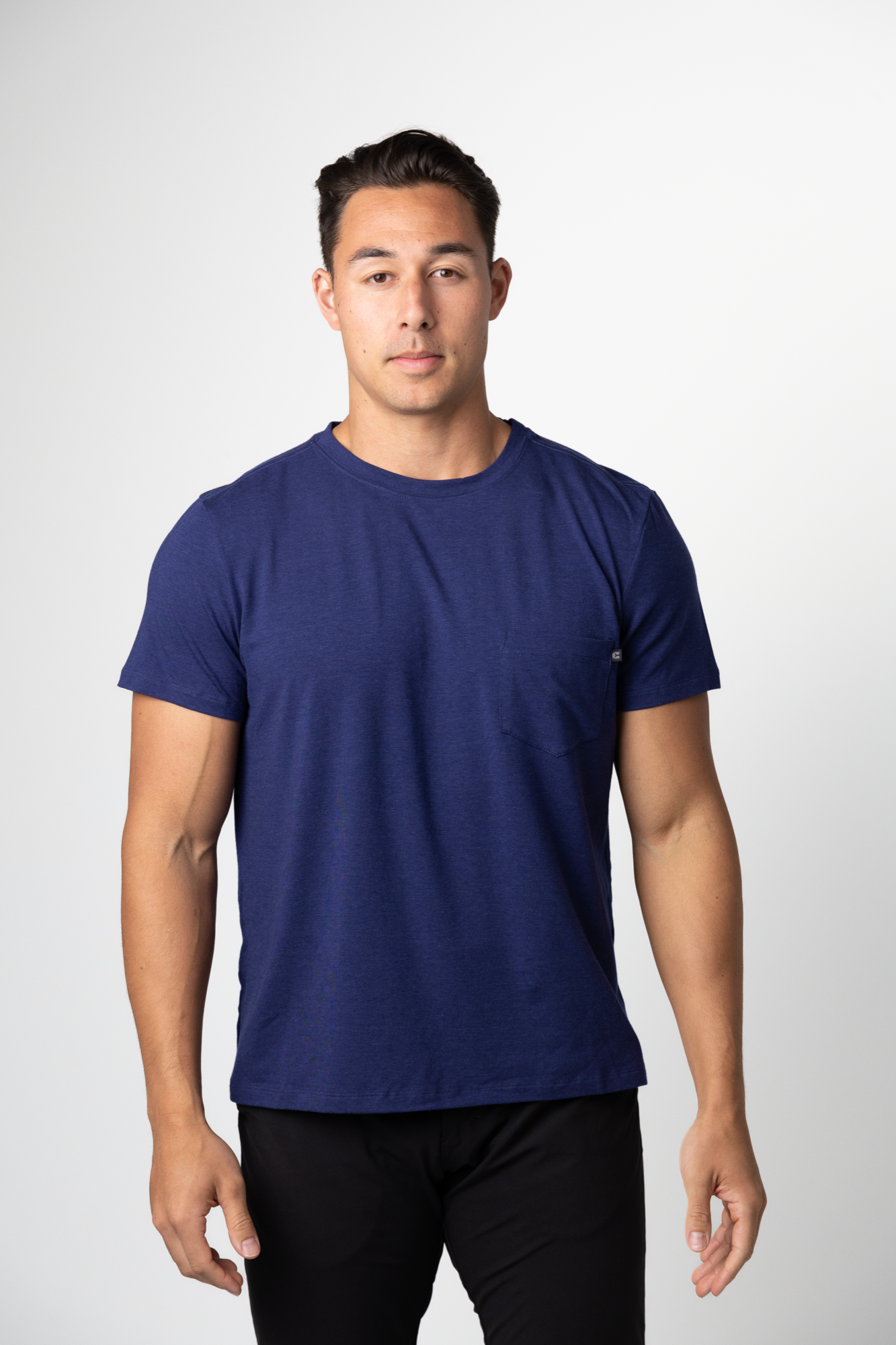 A man with short dark hair stands facing forward against a white background, wearing the Choona Panhandle Pocket Tee and black pants. He has a neutral expression and his arms are relaxed at his sides.