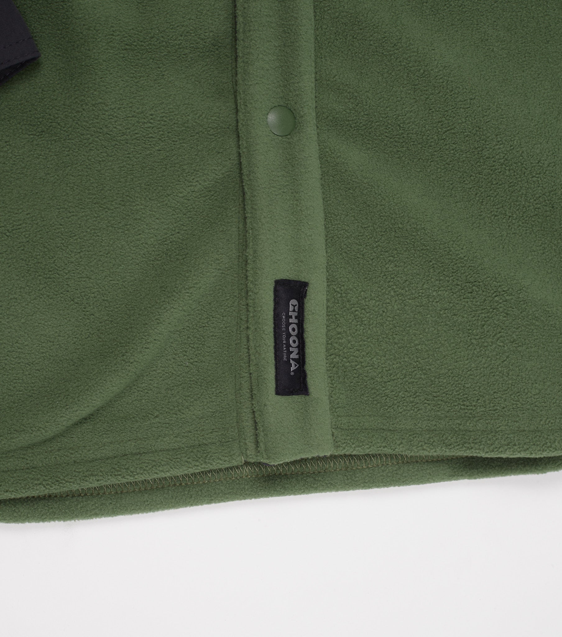 Close-up of Choona’s green Skipper Shacket in recycled polyester, with a black Choona tag and a snap button on the seam, set against a white background.