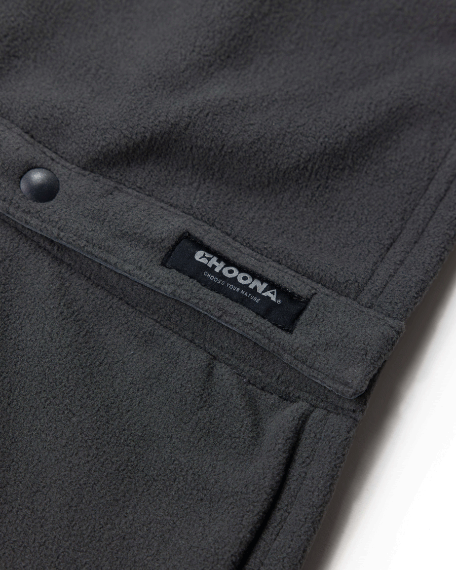 Close-up of a dark gray Skipper Shacket by Choona, crafted from recycled polyester with a snap button, pocket seam, and black label featuring “CHOONA” in white and “CHOOSE YOUR NATURE.” Ideal for cold weather.