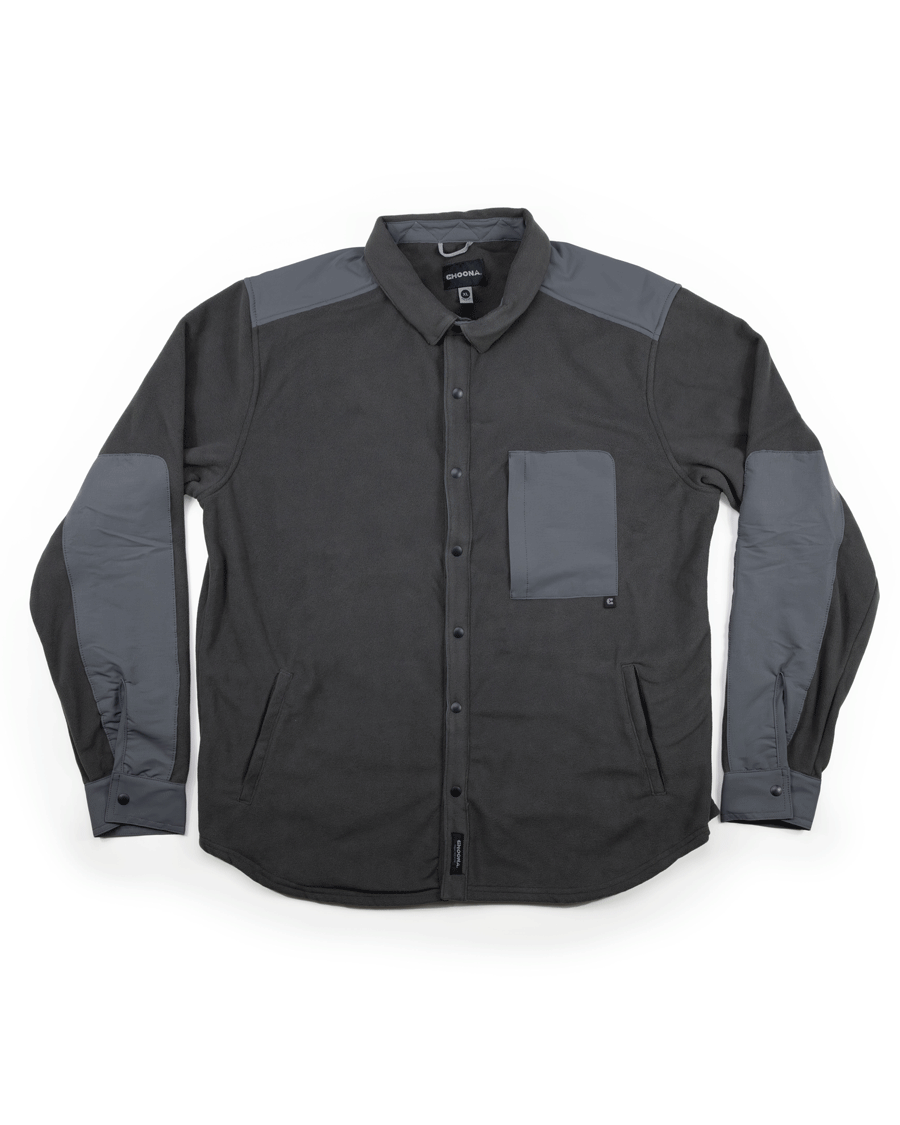 The Choona Skipper Shacket is a long-sleeved, button-up dark gray jacket with lighter gray shoulder, elbow, and chest pocket patches. Made from recycled polyester—ideal for cold weather. Shown laid flat on a white background.