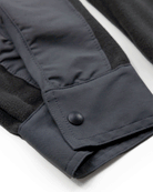 Close-up of a dark gray Choona Skipper Shacket sleeve with a snap button cuff, featuring contrasting textures and stitching—made from recycled polyester for added warmth in cold weather.