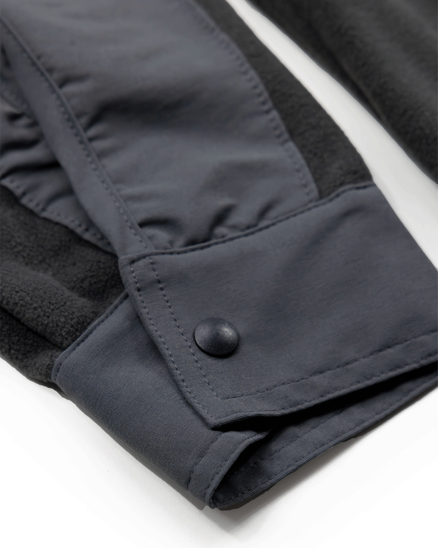 Close-up of a dark gray Choona Skipper Shacket sleeve with a snap button cuff, featuring contrasting textures and stitching—made from recycled polyester for added warmth in cold weather.