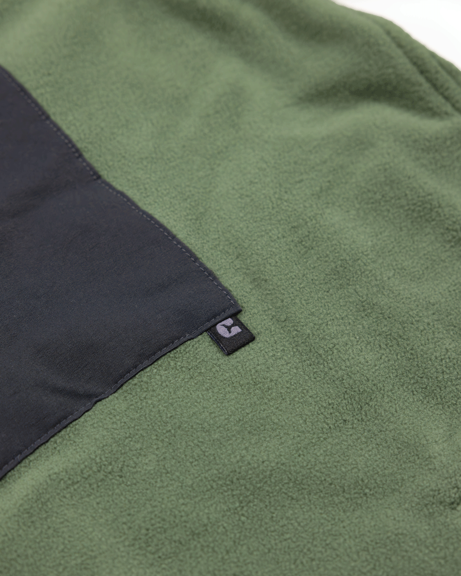 Close-up of Choona’s green fleece, made from recycled polyester, featuring a black rectangular patch and a small black tag with a white C logo—ideal for cold weather or layering under your Skipper Shacket.