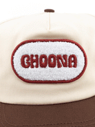 The Choona Fly Patch Snapback is a cream cotton twill cap with a brown brim, featuring a white oval patch outlined in red and embroidered with CHOONA in bold red letters.