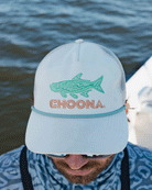 A person wearing the Choona Silver King Snapback with a green fish graphic and CHOONA embroidery, styled with sunglasses and a blue patterned shirt, stands by the water for a cool, relaxed vibe.