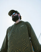 A bearded person in sunglasses, a cap, and the Choona Grayton Ultra-Lightweight Hoodie stands outdoors against a bright sky, photographed from a low angle.