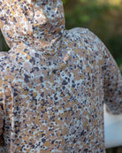 A person outdoors wears the Choona Grayton Ultra-Lightweight Hoodie, featuring a beige, brown, and gray abstract dot pattern. The photo focuses on the back, showcasing the hoodie’s unique fabric design.