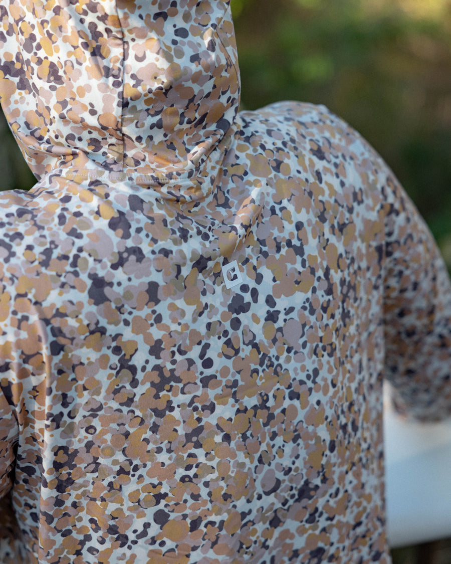 A person outdoors wears the Choona Grayton Ultra-Lightweight Hoodie, featuring a beige, brown, and gray abstract dot pattern. The photo focuses on the back, showcasing the hoodie’s unique fabric design.