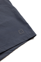 Close-up of the hem of Choonas Shore Short in dark blue, showcasing a small square black rubber logo patch—perfect for coastal adventures with advanced moisture-wicking technology.