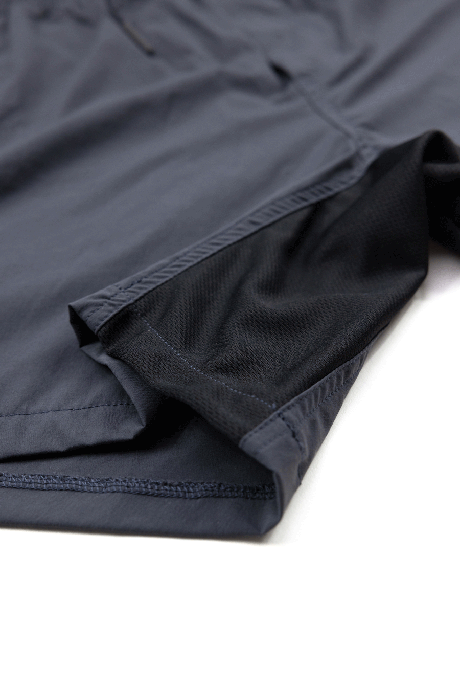 Close-up of Choona Shore Short athletic shorts in navy blue, featuring black mesh lining and detailed stitching. Engineered for coastal activities with advanced wicking technology, shown on a white background.