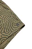 Close-up of Choonas Shore Short fabric, showing an abstract green and olive maze pattern. A small gray square logo with the letter S appears near the hem—perfect for coastal activities.