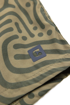 Close-up of Choonas Shore Short fabric: green abstract pattern on khaki, small black square logo with a white shape near the hem. Designed for coastal activities and all-day comfort with advanced wicking technology.