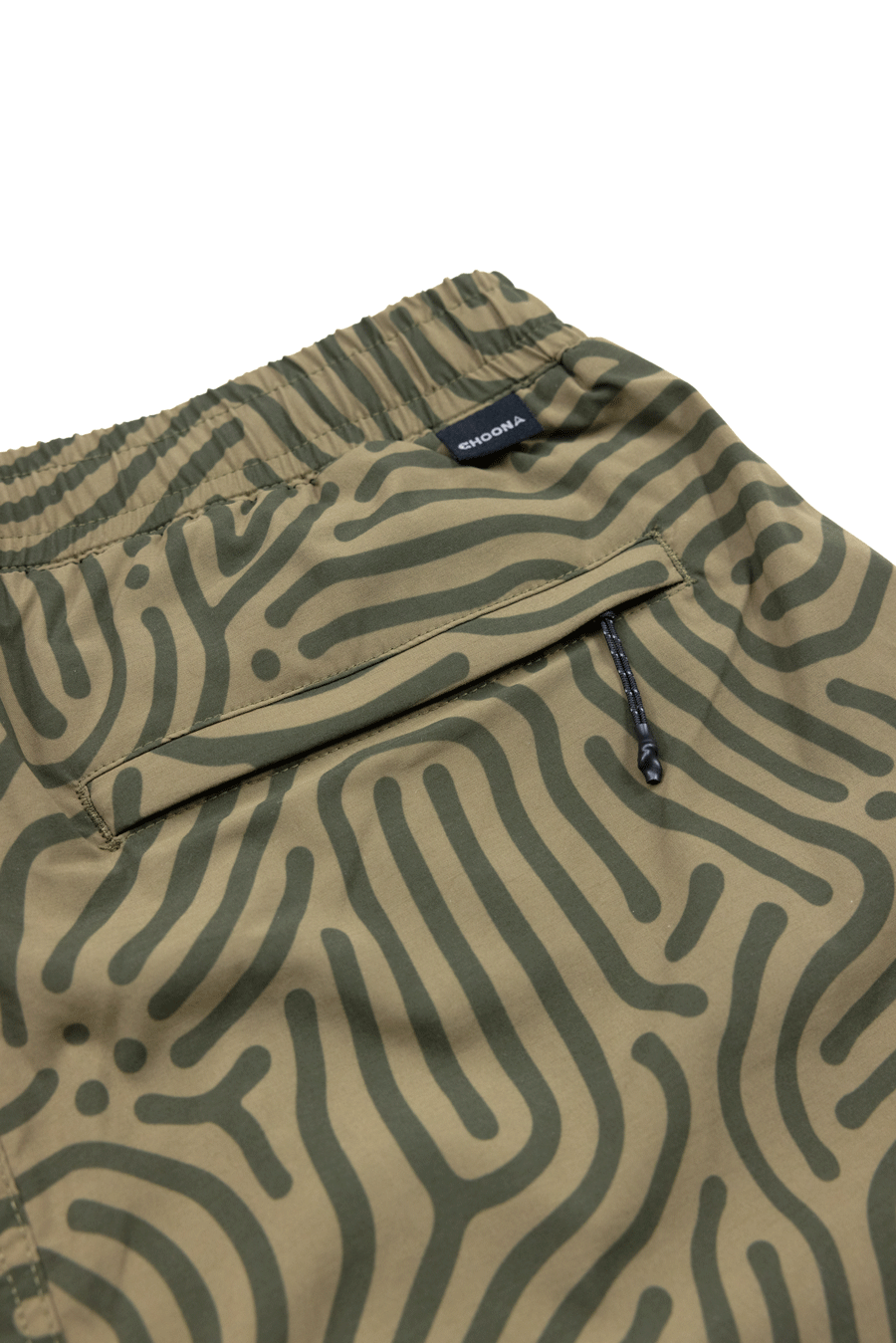 Close-up of Choona Shore Short—green shorts with an abstract wavy line pattern, elastic waistband, zipper pocket, and a small black SINOBIA tag. Perfect for coastal activities with built-in wicking technology.