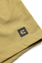Close-up of the light tan Choona Shore Short hem, showcasing a small black square logo with a stylized “C”—ideal for coastal activities due to advanced wicking technology.
