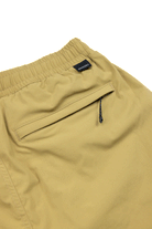Close-up of the back of tan Choona Shore Short pants with an elastic waistband, zippered pocket with black pull, and a small black tag with white text—perfect for coastal activities.