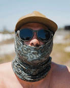 A person in a tan cap, dark sunglasses, and a Choona Grayton Sun Mask made of ultra-breathable fabric stands outdoors on a sunny day with a blurred natural background.