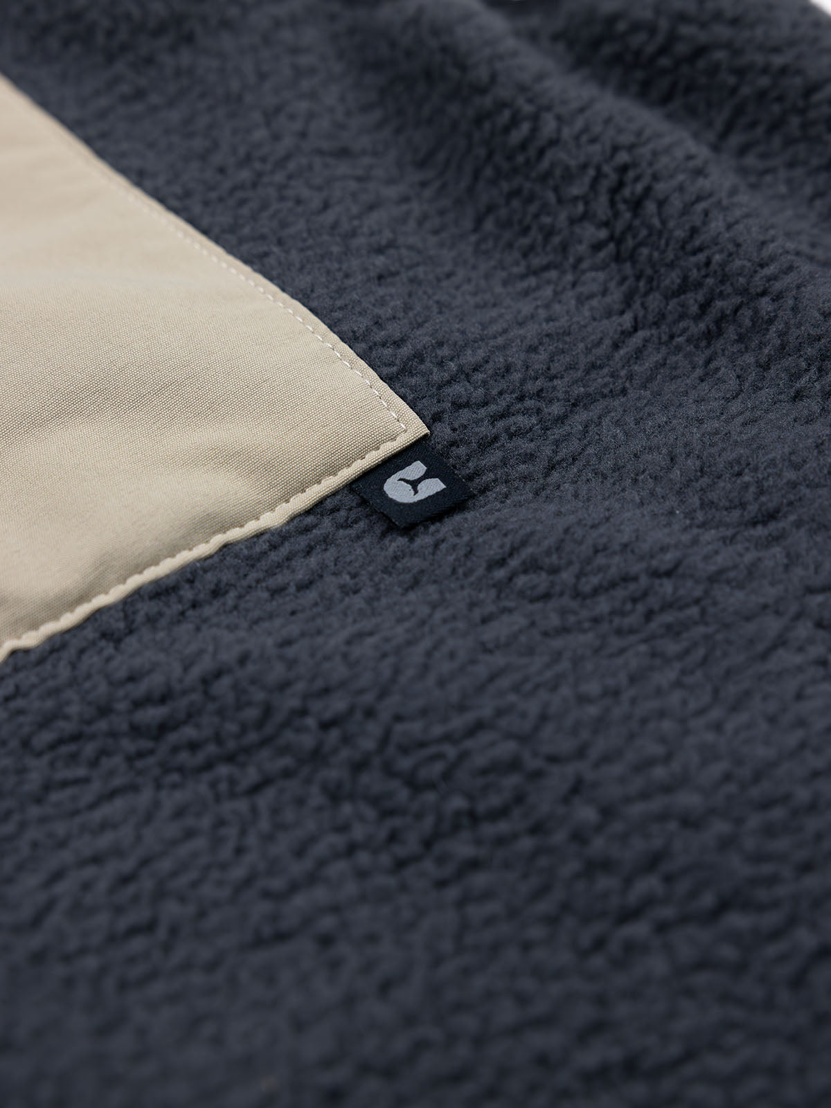 Close-up of the Choona Pt. Washington Sherpa Vest in dark gray high pile fleece, featuring a beige rectangular patch and a small black tag with a white logo for a cozy look.
