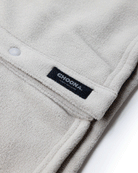 Close-up of the cream-colored Choona Skipper Shacket fleece, made from recycled polyester with a snap button and black label, shown on a white background—the perfect cold weather piece.