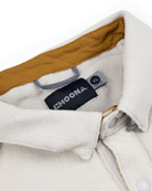 Close-up of the Choona Skipper Shacket in cream fleece made from recycled polyester, with a mustard yellow inner collar, snap buttons, and a black CHOONA label—a cozy layer for cold weather.