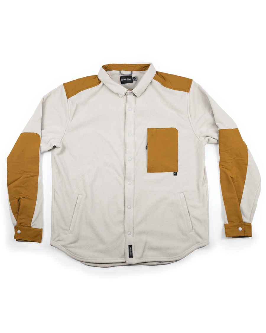 The Choona Skipper Shacket is a long-sleeve, off-white button-up with tan patches on the shoulders, elbows, cuffs, and chest pocket. Made from recycled polyester, it features a collar and snap front, ideal for cold weather.