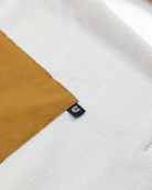 A close-up of Choonas Skipper Shacket in white recycled polyester fleece, featuring a mustard yellow rectangular patch and a small black tag with a white C—an ideal piece for cold weather.