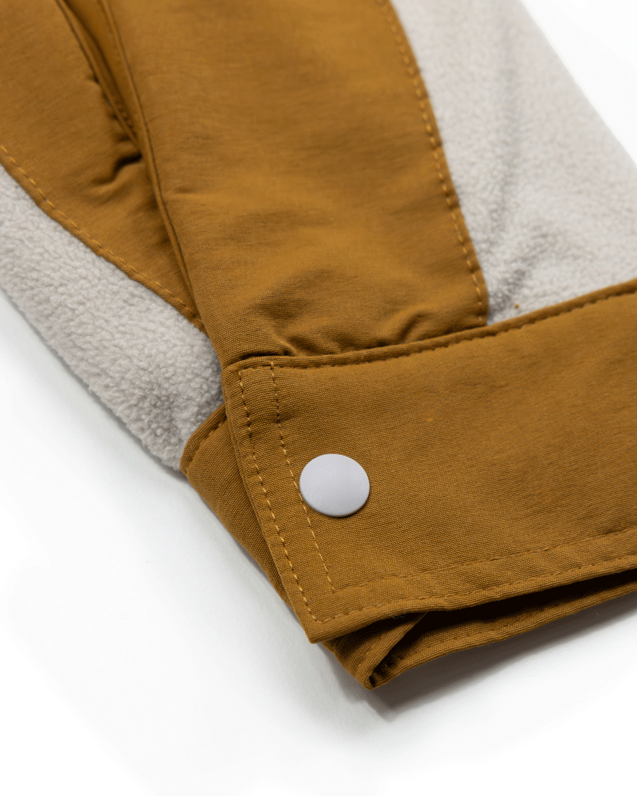 Close-up of the cuff on Choonas Skipper Shacket in brown and light gray, featuring a white snap button. The soft fabric includes a fleece-like recycled polyester gray section—ideal for cold weather.