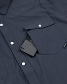 A close-up of a dark blue Choona Panhandle Pearl Snap shirt with white buttons and a front pocket, partially showing a black textured wallet—perfect for that coastal cowboy style.