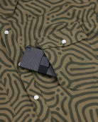 A black textured wallet peeks out of the chest pocket of a Choona Panhandle Pearl Snap—a green, maze-patterned shirt with white snaps, perfect for a coastal cowboy look.