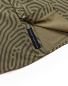 A close-up of olive-green fabric with black wavy patterns and a CHOOSE YOUR NATURE tag showcases the Choona Panhandle Pearl Snap, hinting at its signature pocket and inner lining for a unique coastal cowboy style.