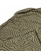 Close-up of the Choona Panhandle Pearl Snap shirt in green, featuring an abstract wavy dark green pattern and a collar. The coastal cowboy style shirt is laid flat on a white background.