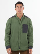 A man wears the Choona Skipper Shacket—a green fleece jacket with recycled polyester and dark gray accents on the shoulders, pocket, and cuffs—standing against a plain white background. Perfect for cold weather.