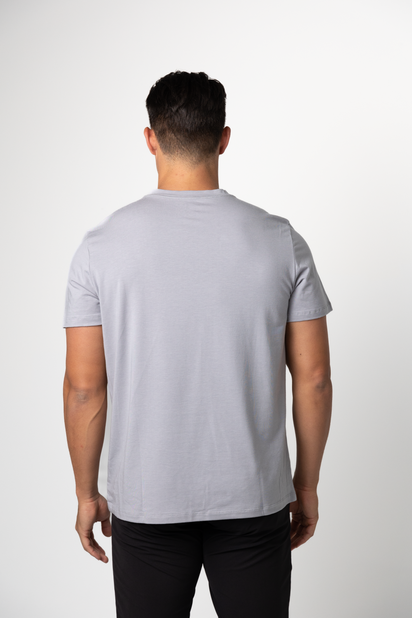 A man with short dark hair, seen from behind, wears a light gray Choona Panhandle Pocket Tee made from a sustainable Lyocell blend and black pants against a plain white background.